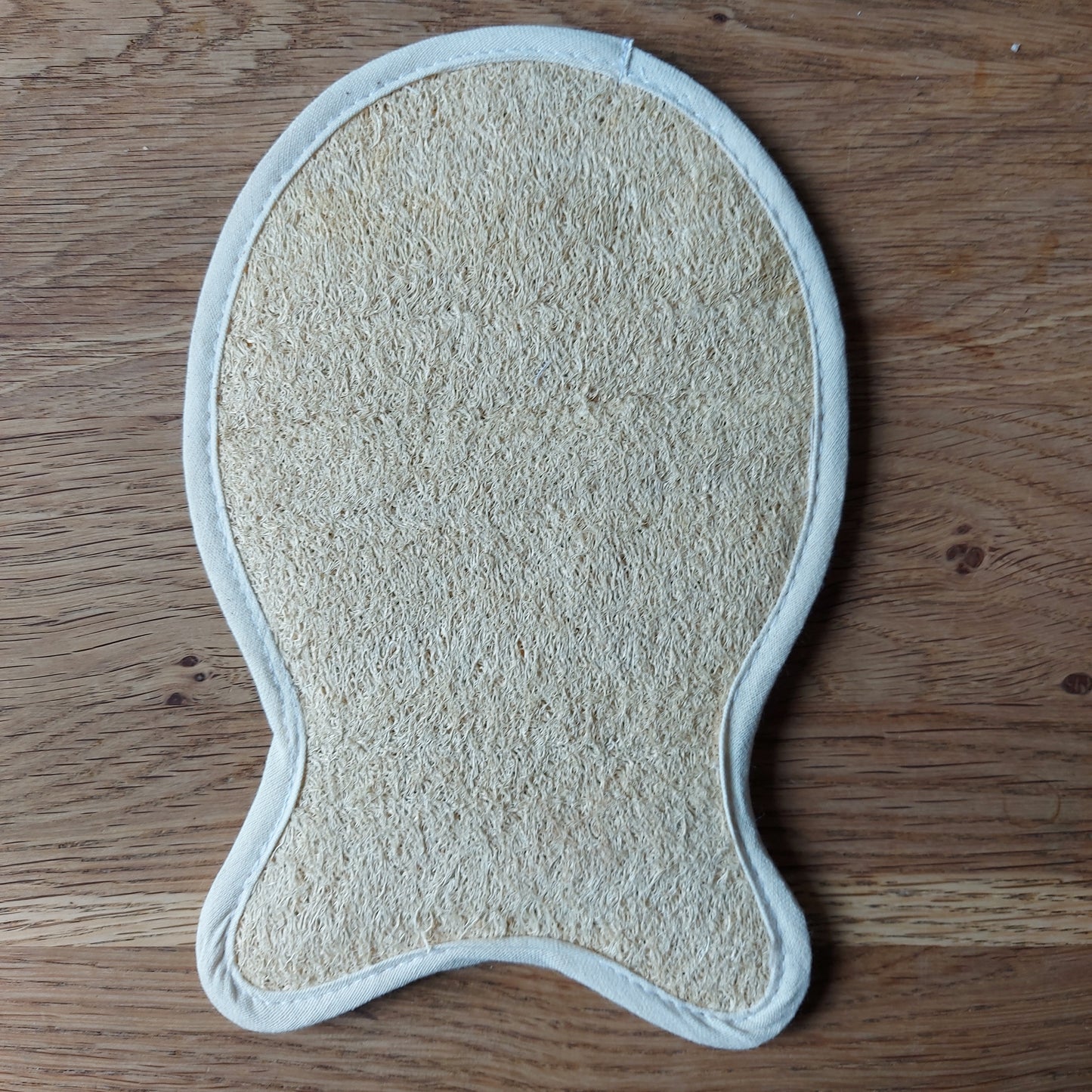 Une éponge naturelle en luffa transformée en gant de massage en forme de poisson est posée sur une table en bois. Disponible chez ILELI savons Orsay, Eponge Loofah naturel "Poisson", Massage naturel, produit de bain biodégradable, salle de bain zéro déchet