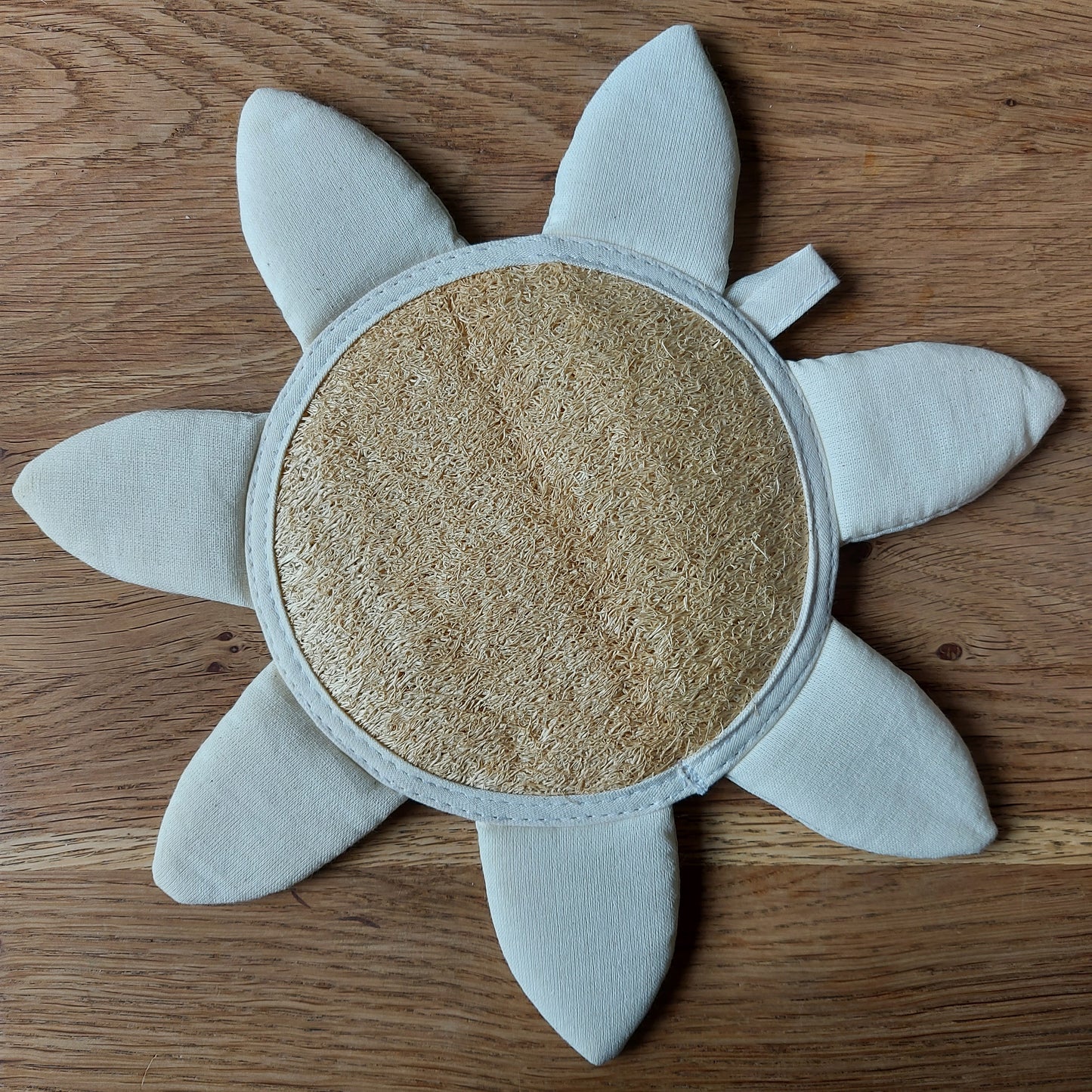 Une jolie éponge de luffa en forme de soleil ou de fleur est posée sur une table en bois. C'est le jouet de bain idéal pour les petits enfants. Salle de bain zéro déchet - gant de massage naturel et bio-dégradable. Produit de ILELI savons Orsay