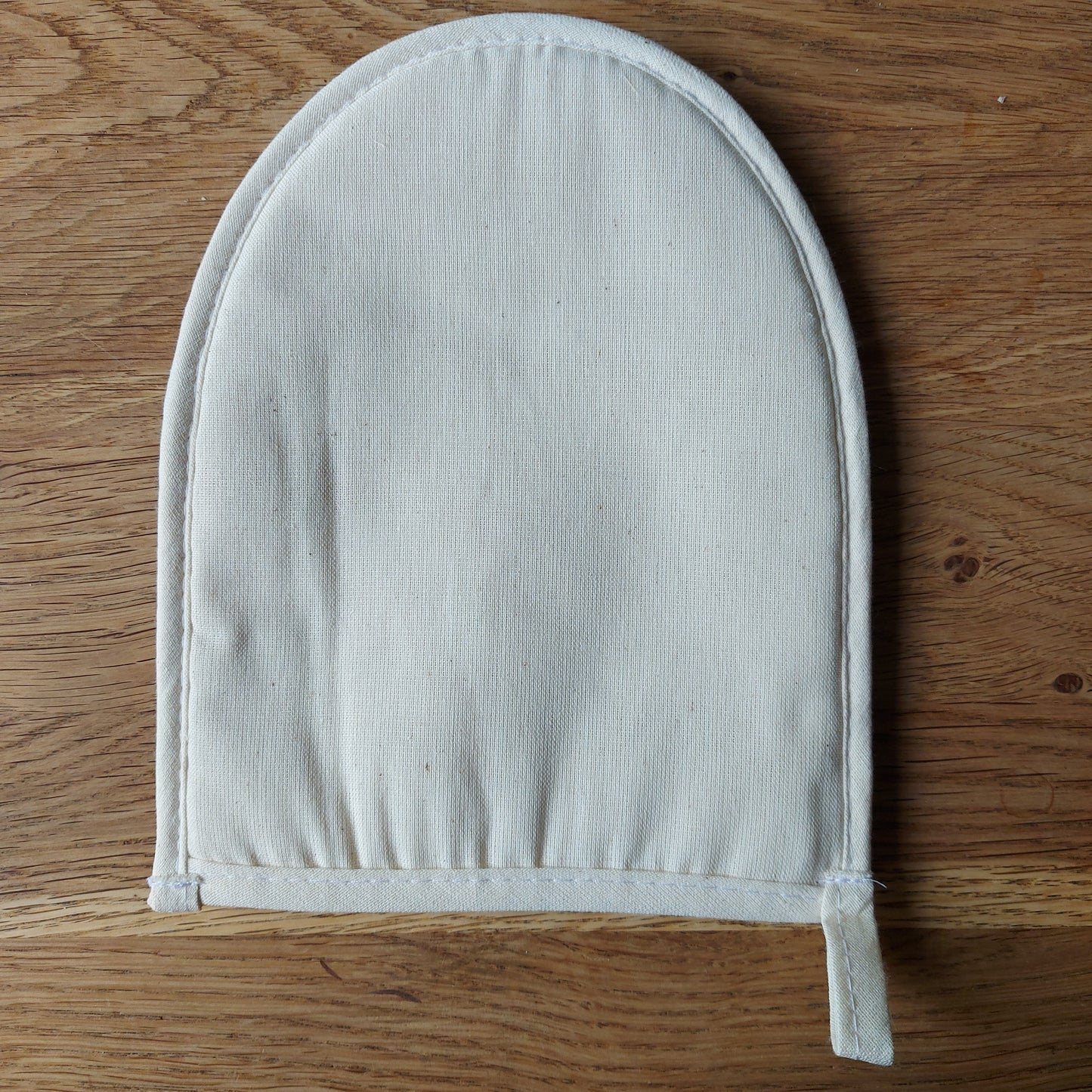 Pour salle de bain zéro déchet - gant de massage naturel et bio-dégradable. Une éponge naturelle en loofah transformée en gant de massage est posée sur une table en bois. Disponible chez ILELI savons Orsay