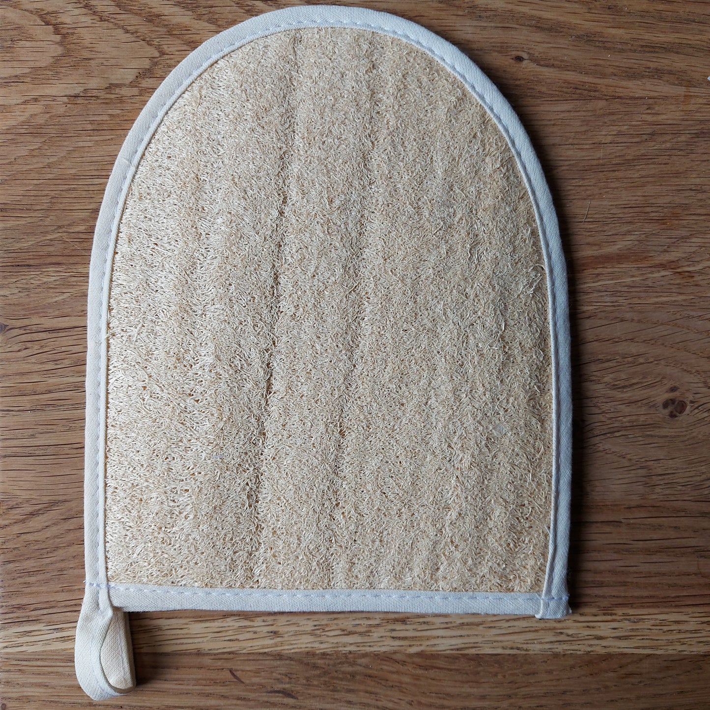 Une éponge naturelle en loofah transformée en gant de massage est posée sur une table en bois. Disponible chez ILELI savons Orsay - Salle de bain zéro déchet - gant de massage naturel et bio-dégradable.