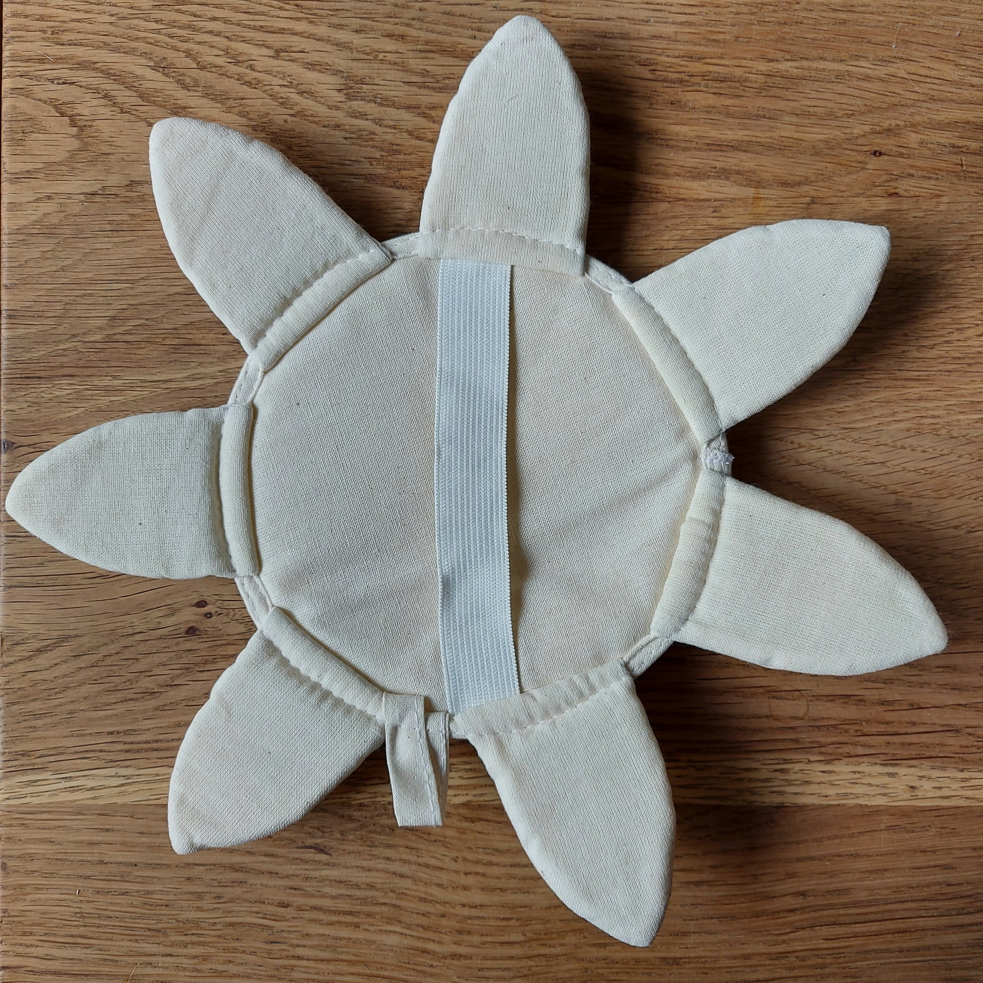 Une jolie éponge de luffa en forme de soleil ou de fleur est posée sur une table en bois. C'est le jouet de bain idéal pour les petits enfants. Produit de ILELI savons Orsay Salle de bain zéro déchet - gant de massage naturel et bio-dégradable, convient également comme porte-savon. Cotton bio et luffah