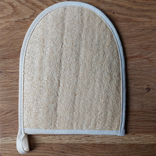 Une éponge naturelle en loofah transformée en gant de massage est posée sur une table en bois. Disponible chez ILELI savons Orsay - Salle de bain zéro déchet - gant de massage naturel et bio-dégradable.